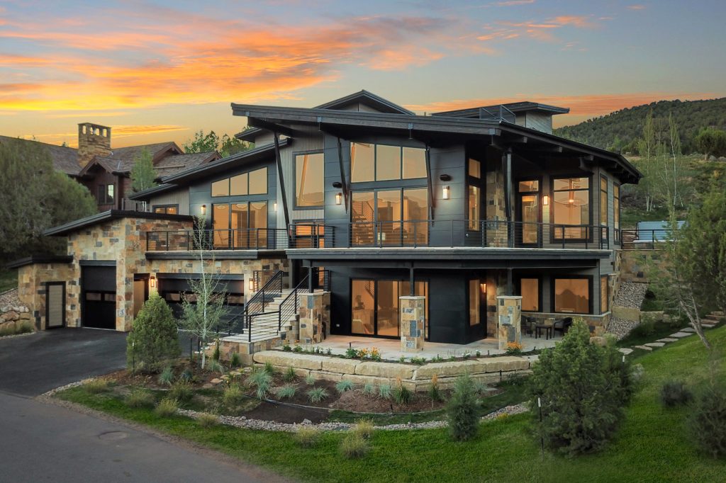 Modern luxury home built by H&C Construction in Colorado featuring expansive windows, natural stonework, and a multi-level design at sunset