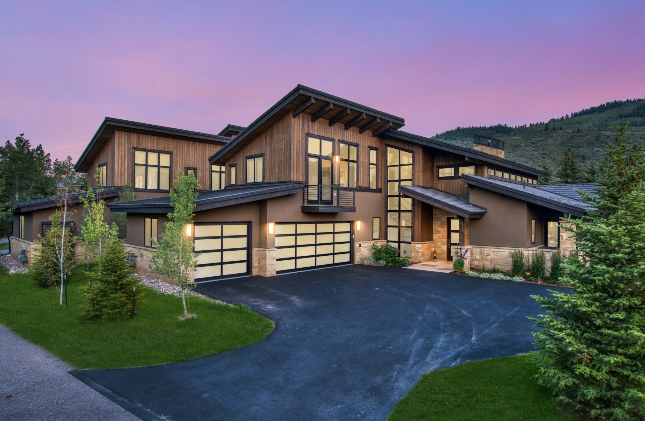 Contemporary mountain duplex built by H&C Construction in Arrowhead, Colorado, featuring wood and stone siding, large windows, and modern garage doors